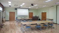The lecture room is equipped with desks, chairs, a projector, and other equipment that can be used for meetings. The room is large enough to accommodate about 200 people.