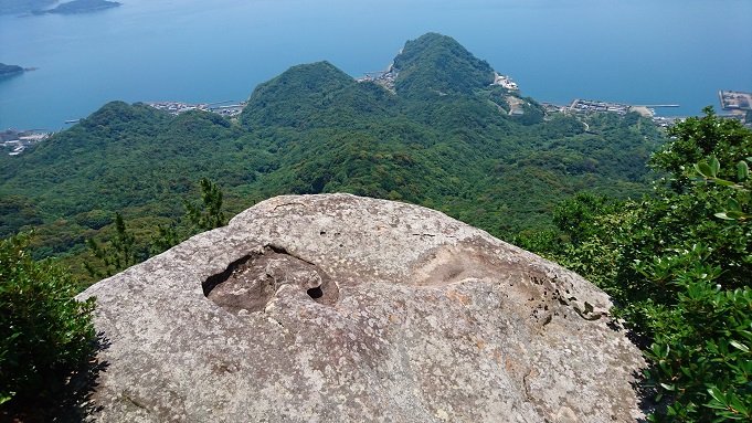山頂から見下ろした風景で、手前にハート型のくぼみがある巨大な岩、背景に、山の裾野と海が広がっている（２０２１年６月撮影）