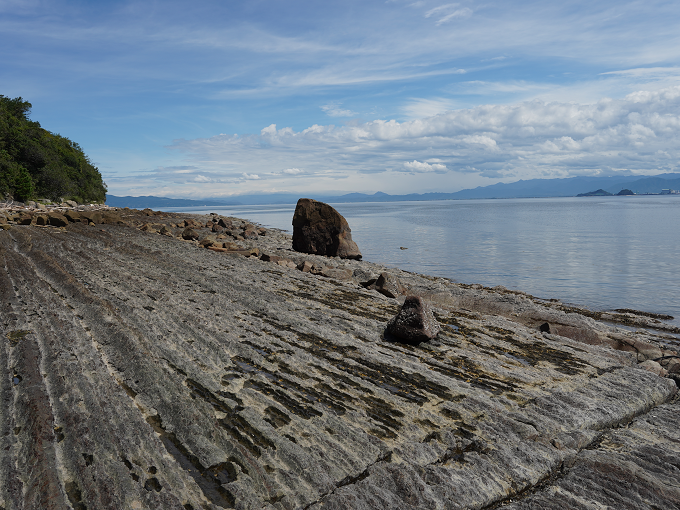 左下から右上に向かって洗濯板のように折り重なるように連なる板状の岩の先に海が広がる風景を撮影した写真