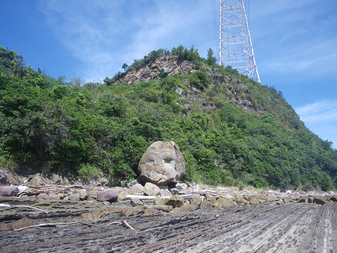 頂上に鉄塔がそびえ立つ小高い山とそのふもとにある人面岩が映された写真
