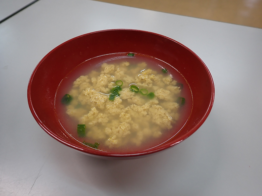 そぼろ状に固まった黄色いカニのすり身と青ネギが入った汁