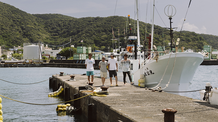 古仁屋漁港の突堤の上を４人の男性が歩いている